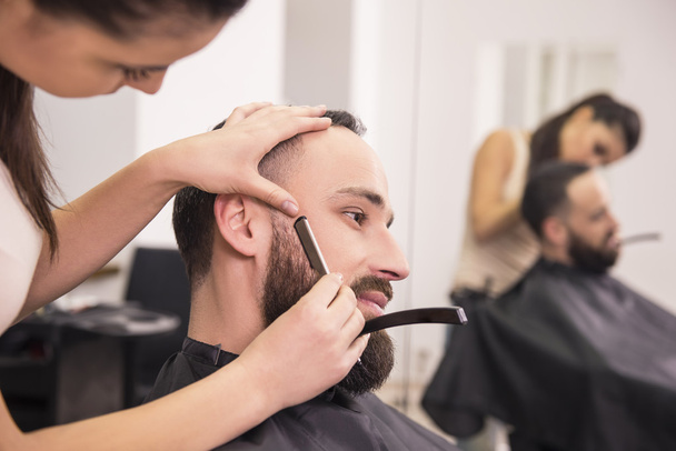 Hairdresser shaving an old-fashioned razor of satisfied client in professional hairdressing salon. - Foto, Imagem