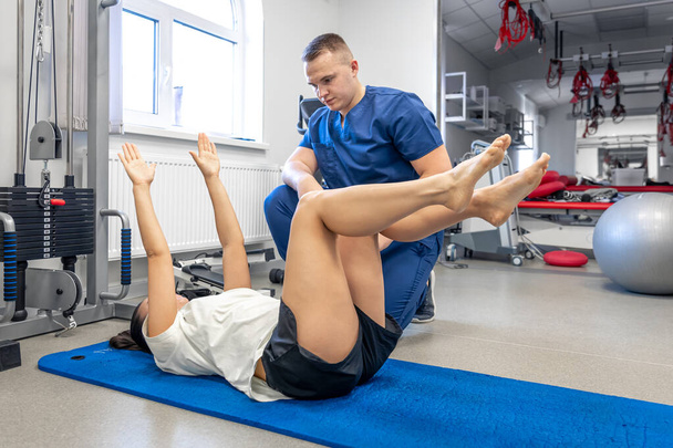 Женщина лежит на коврике для йоги и занимается гимнастикой с помощью своего молодого физиотерапевта, концепция физиотерапии для людей с травмами. - Фото, изображение