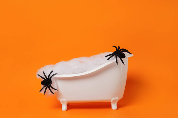 Bañera de Halloween llena de tela de araña y arañas negras sobre fondo naranja brillante. Un concepto aterrador. Podio para productos - Foto, Imagen