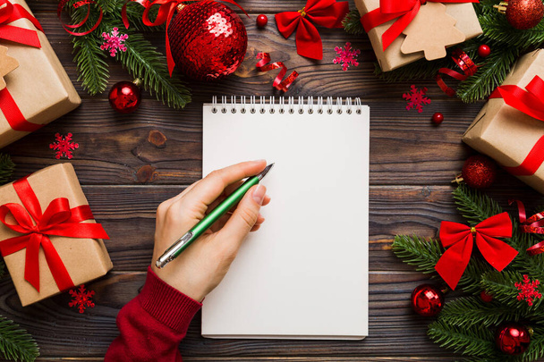 Nainen kirjoittaa joulua tehdä lista muistikirja värillinen tausta joulu koristeet. - Valokuva, kuva