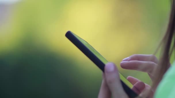 Close-up of the hands of a girl with holding her mobile phone with trees in the background. Selective focus - Footage, Video