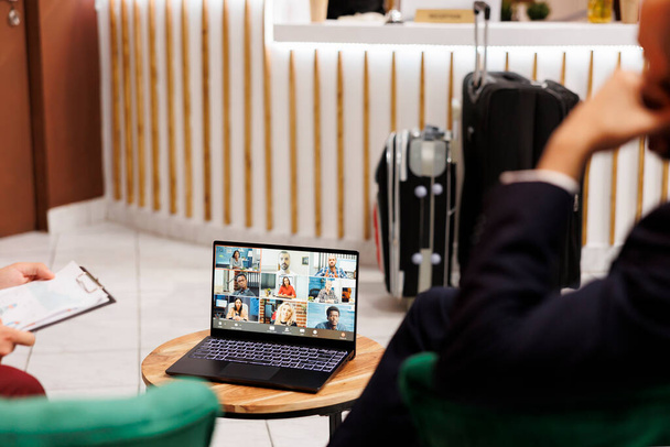 People attend business meeting in lobby, sitting at hotel lounge area with telework conference online on laptop. Management team discussing with colleagues on videocall remote, front desk. - Photo, Image