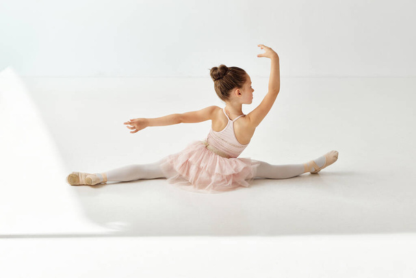 Visszapillantás portré a kis imádnivaló balerina táncos lány ül zsinórban és rózsa tutu ruha a táncteremben, szemben a fehér stúdió háttér. A szépség, a divat, a hobbi, a gyerekbalett fogalma. hirdetés - Fotó, kép