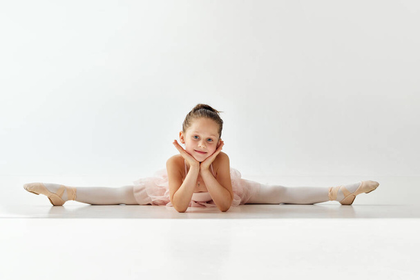 Küçük şirin balerin kız portresi dans salonundaki ipli ve tutu bale elbisesiyle beyaz stüdyo arka planında oturuyor. Güzellik, moda, hobi, çocuk balesi kavramı. ad - Fotoğraf, Görsel