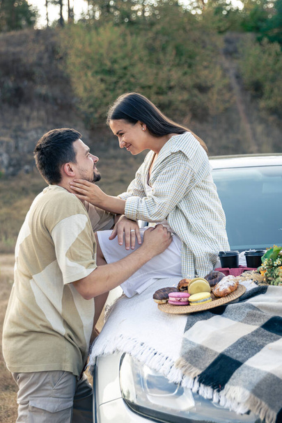 Krásný mladý pár si užívá piknik na západě slunce na louce, opírající se o módní auto, muž a žena si užívají. - Fotografie, Obrázek