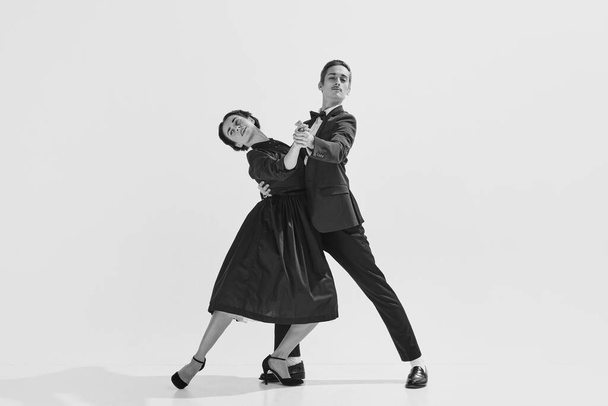 Black and white. Passion and love. Beautiful young woman and man in stylish clothes dancing on white background. Concept of hobby, retro dance, vintage style, choreography, beauty. Monochrome art. Ad - Foto, Bild