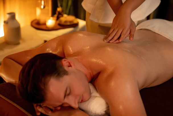 Homme caucasien client appréciant relaxant massage spa anti-stress et dorloter avec beauté loisirs de la peau dans la bougie chaude éclairage spa salon ambiant à la station de luxe ou hôtel. Tranquillité - Photo, image