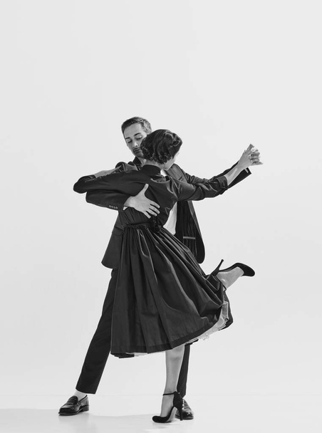 Rhythm and freedom. Black and white. Beautiful young woman in elegant black dress dancing with stylish and handsome man. Concept of hobby, retro dance, vintage style, choreography. Monochrome art. Ad - Photo, Image