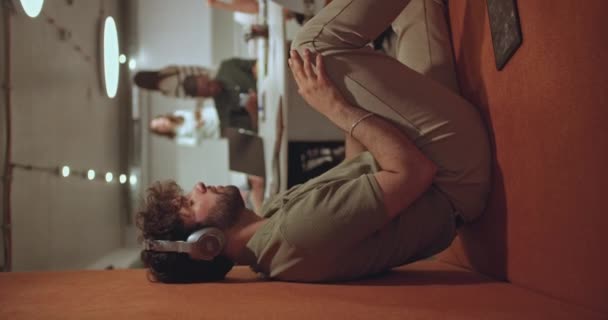 Szczęśliwy, pozytywny, męski pracownik słuchający muzyki na słuchawkach i tańczący podczas przerwy w pracy, siedzący we wnęce na ścianie w nowoczesnym warsztacie biurowym. - Materiał filmowy, wideo