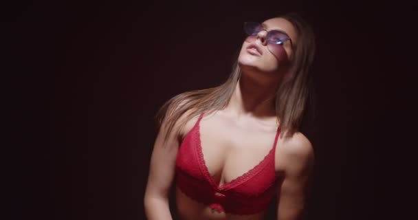 Hermosa chica cool bailando sensualmente, usando lencería de ropa interior roja y gafas de sol aisladas en negro, cámara lenta - Metraje, vídeo