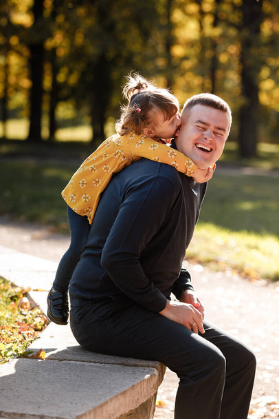 Joyful dad hugs his little smiling daughter. Single daddy and child have fun, laugh and enjoy nature outdoors at autumn park. Concept of parental care and happy carefree childhood. Happy fathers day. - Photo, Image
