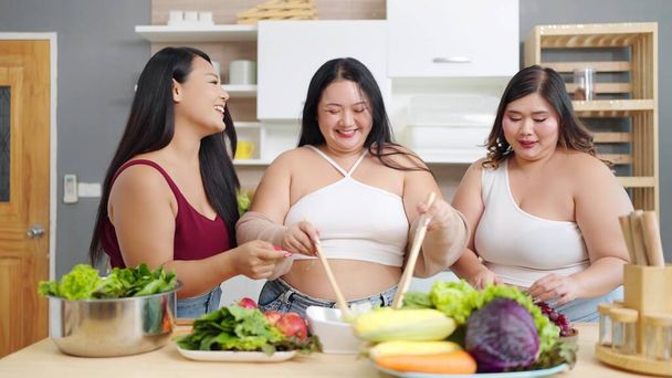 Egy csapat vidám ázsiai plusz méretű nő szeret főzni, vacsorát készíteni otthon a konyhában. Testpozitivitás. Testelfogadási koncepció - Fotó, kép