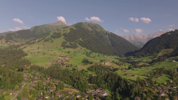Luftaufnahme einer panoramischen Landschaft. Häuser und Chalets auf Bergwiesen und hochalpine Gipfel im Hintergrund. Gstaad, Schweiz. - Filmmaterial, Video