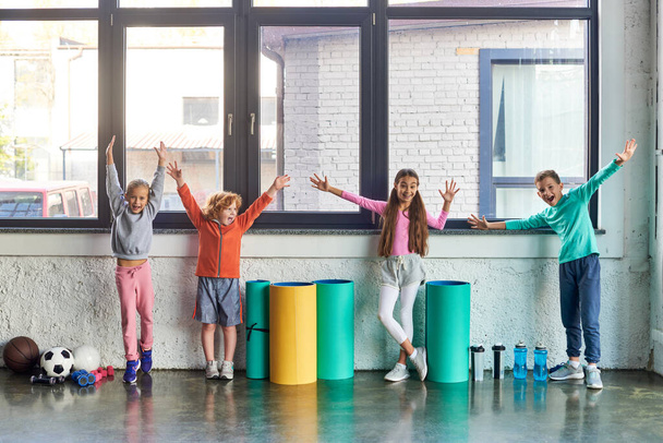 cuatro lindos niños preadolescentes en ropa deportiva que se divierten y sonríen en el gimnasio, deporte infantil - Foto, Imagen
