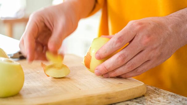 In the welcoming setting of a modern kitchen, a young man continues his dinner preparation process. Hes currently involved in slicing yellow onions into rings, prepping them for grilling on an - Photo, Image