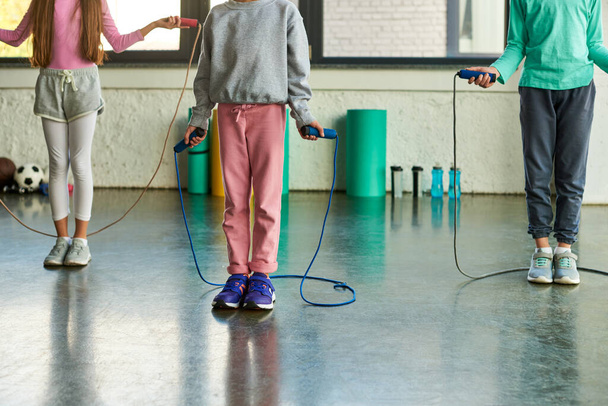 bijgesneden beeld van drie preadolescente kinderen in sportkleding met springtouwen, kindersport - Foto, afbeelding