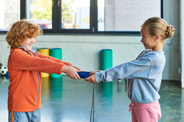 cute red haired boy and blonde girl holding jump rope and looking at each other, child sport - Photo, Image