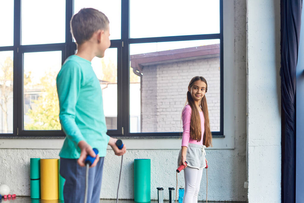 pretty preadolescent children with skipping ropes in hands smiling at each other, child sport - Photo, Image