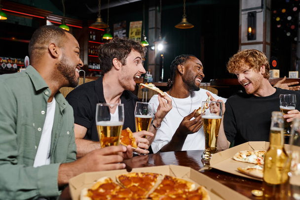 csoport négy boldog fajok közötti barátok eszik pizza és sört iszik a bárban, férfiak legénybúcsú - Fotó, kép