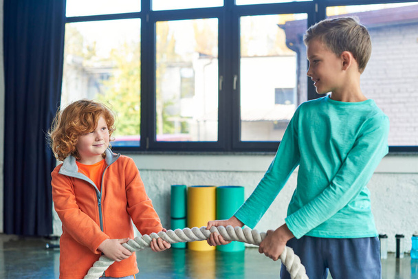 két serdülő fiú sportruházatban húzza a fitneszkötelet és mosolyog egymásra, gyermeksport - Fotó, kép