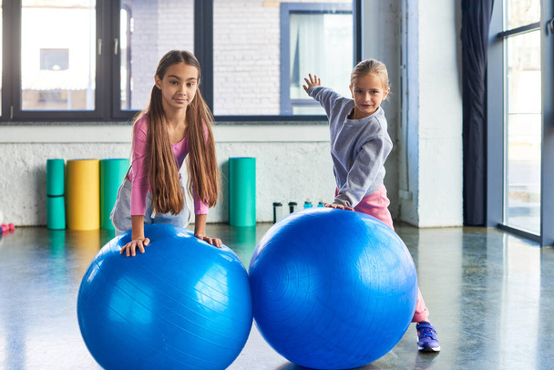 pretty preadolescent girls posing next to fitness balls and looking at camera, child sport - Photo, Image