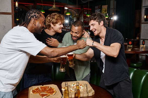 heureux interracial mâle amis poing bumping tandis que toasting verres de bière dans bar, enterrement de vie de garçon - Photo, image