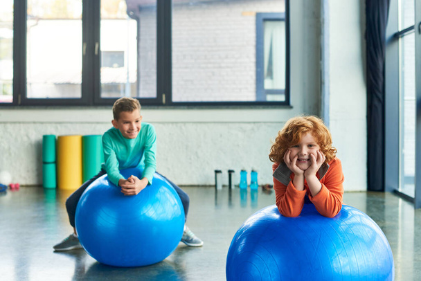 two joyful preadolescent boys exercising on fitness balls and smiling cheerfully, child sport - Photo, Image