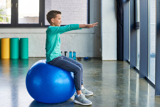 cute preadolescent boy in blue sportswear stretching and training on fitness ball, child sport - Photo, Image