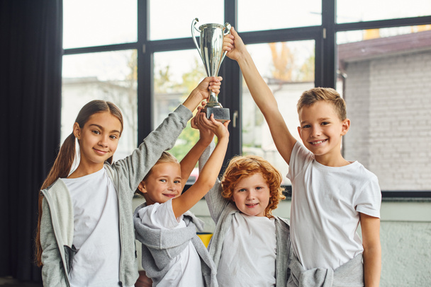 cheering preadolescent boys and girls in sportswear raising trophy above heads, child sport - Photo, Image