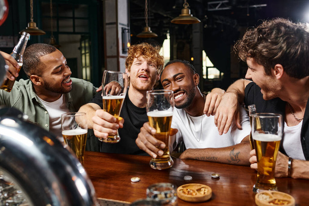 vier glückliche multiethnische Männer mit Biergläsern während des Junggesellenabschieds, männliche Freunde in der Bar - Foto, Bild
