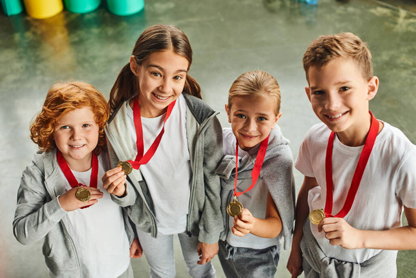 négy serdülő aranyos gyerekek sportruházat mutatja aranyérem a kamera, gyermek sport - Fotó, kép