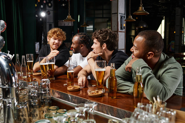 gruppo di uomini multiculturali che passano del tempo insieme, chiacchierando e bevendo birra, amici maschi nel bar - Foto, immagini