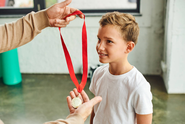 обрезанный вид человека, награждение золотой медалью преклонного возраста симпатичного мальчика в спортивной одежде, детском спорте - Фото, изображение