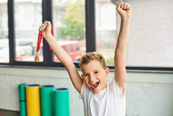 joyful preadolescent boy cheering and holding golden metal, smiling happily at camera, child sport - Photo, Image