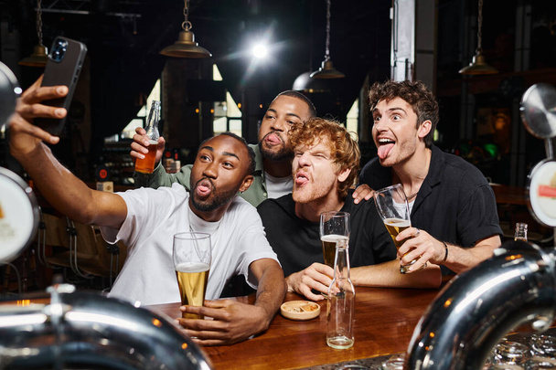 funny multicultural men taking selfie on smartphone while sticking tongue during bachelor party - Photo, Image