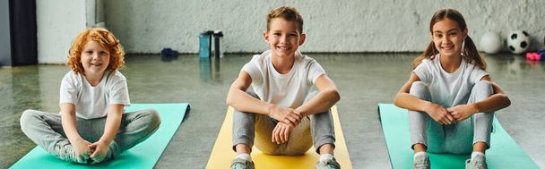 cheerful little boys and girl sitting on fitness mats and smiling at camera, child sport, banner - Photo, Image