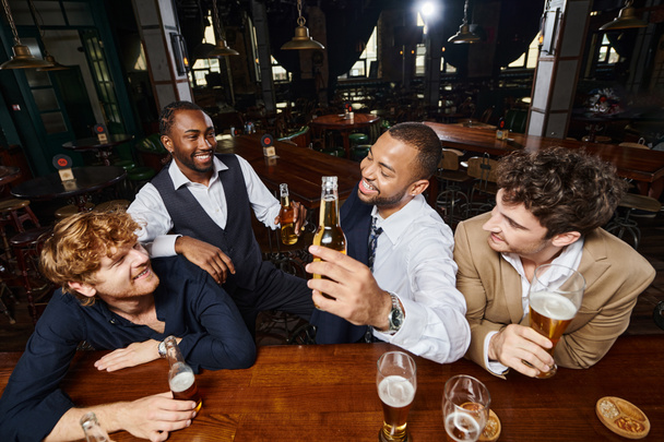 szczęśliwi koledzy w formalnym ubraniu rozmawiający i pijący piwo w barze, spędzający razem czas po pracy - Zdjęcie, obraz