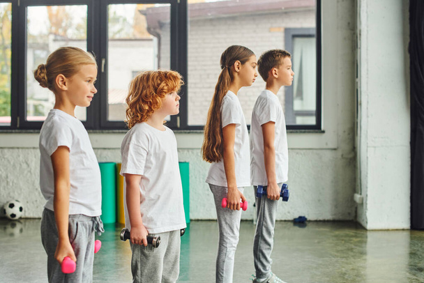 preadolescent jongens en meisjes poseren in profiel in de sportschool met halters in hun handen, kind sport - Foto, afbeelding