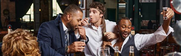pancarta de hombres divertidos y borrachos multiculturales en ropa formal beber tequila en el bar después del trabajo - Foto, Imagen