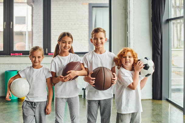 crianças alegres segurando diferentes tipos de bolas e sorrindo para a câmera, esporte infantil - Foto, Imagem
