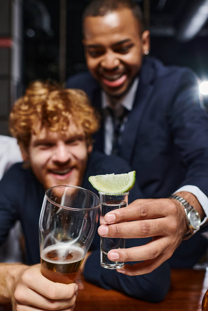 dva různé kolegové cinkání s brýlemi po práci v baru, tequila shot a sklenice piva - Fotografie, Obrázek