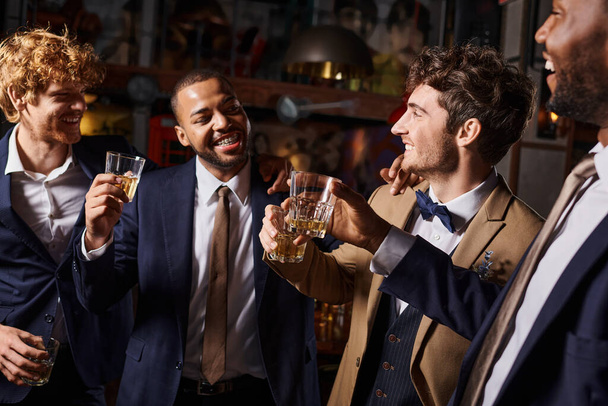 Junggesellenabschied, glückliche interrassische Männer, die mit Gläsern Whiskey in der Bar anstoßen, Bräutigam und Trauzeugen - Foto, Bild