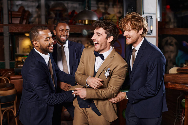 bachelor party, excited interracial men congratulating friend in bar, best men and groom in suits - Photo, Image