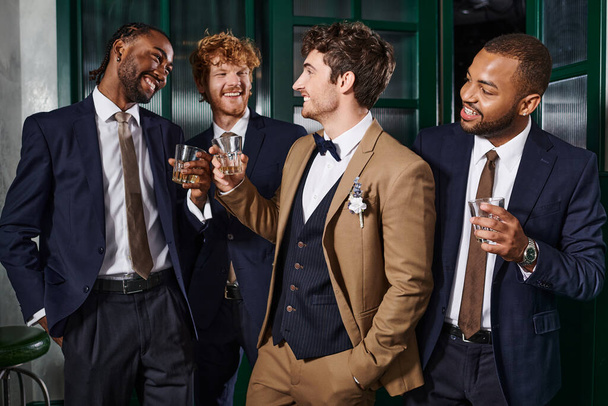 despedida de soltero, multiétnicos mejores hombres tostando vasos de whisky con elegante novio en el bar - Foto, imagen