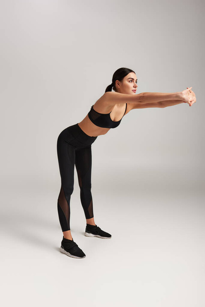 donna atletica in abbigliamento sportivo nero con fitness tracker sul polso che si estende indietro su sfondo grigio - Foto, immagini