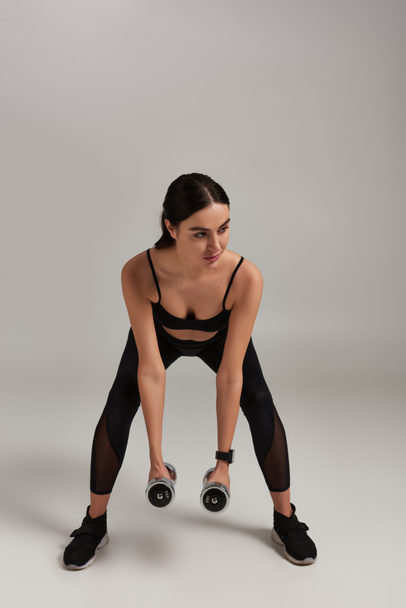 teljes hossza erős nő aktív kopás emelő súlyzók edzés közben szürke háttér - Fotó, kép