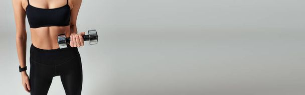 обрізана струнка спортсменка в активному носінні підйомного гантелі під час роботи на сірому тлі, банер - Фото, зображення