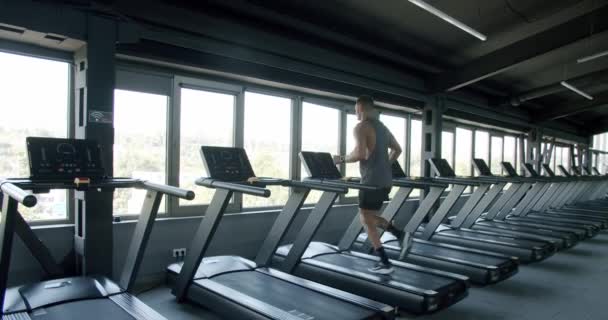 Modern fitness kulübünde koşu bandında koşan atletik bir adam. Genç sporcu erkek spor salonunda kardiyo eğitimi alıyor ve koşuyor. Etkin yaşam tarzı kavramı - Video, Çekim