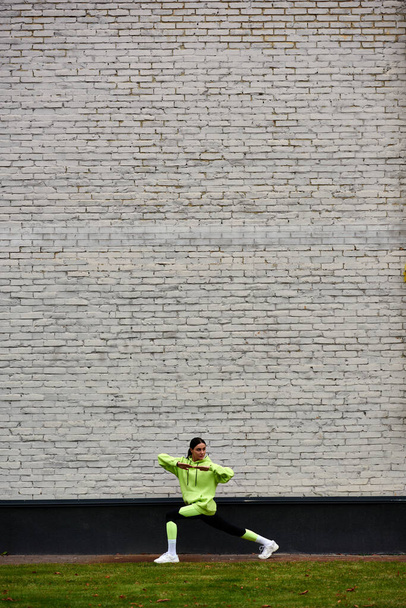 esportista ativo na cor de limão com capuz e leggings fazendo lunges durante o exercício ao ar livre - Foto, Imagem