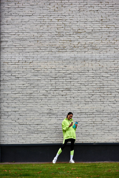 χαρούμενη αθλήτρια με κουκούλα και κολάν χρησιμοποιώντας smartphone και στέκεται με μπουκάλι με νερό - Φωτογραφία, εικόνα